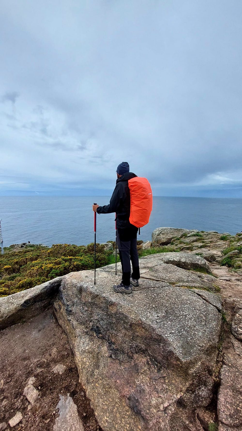 A walker with a backpack standing on a rock by the sea