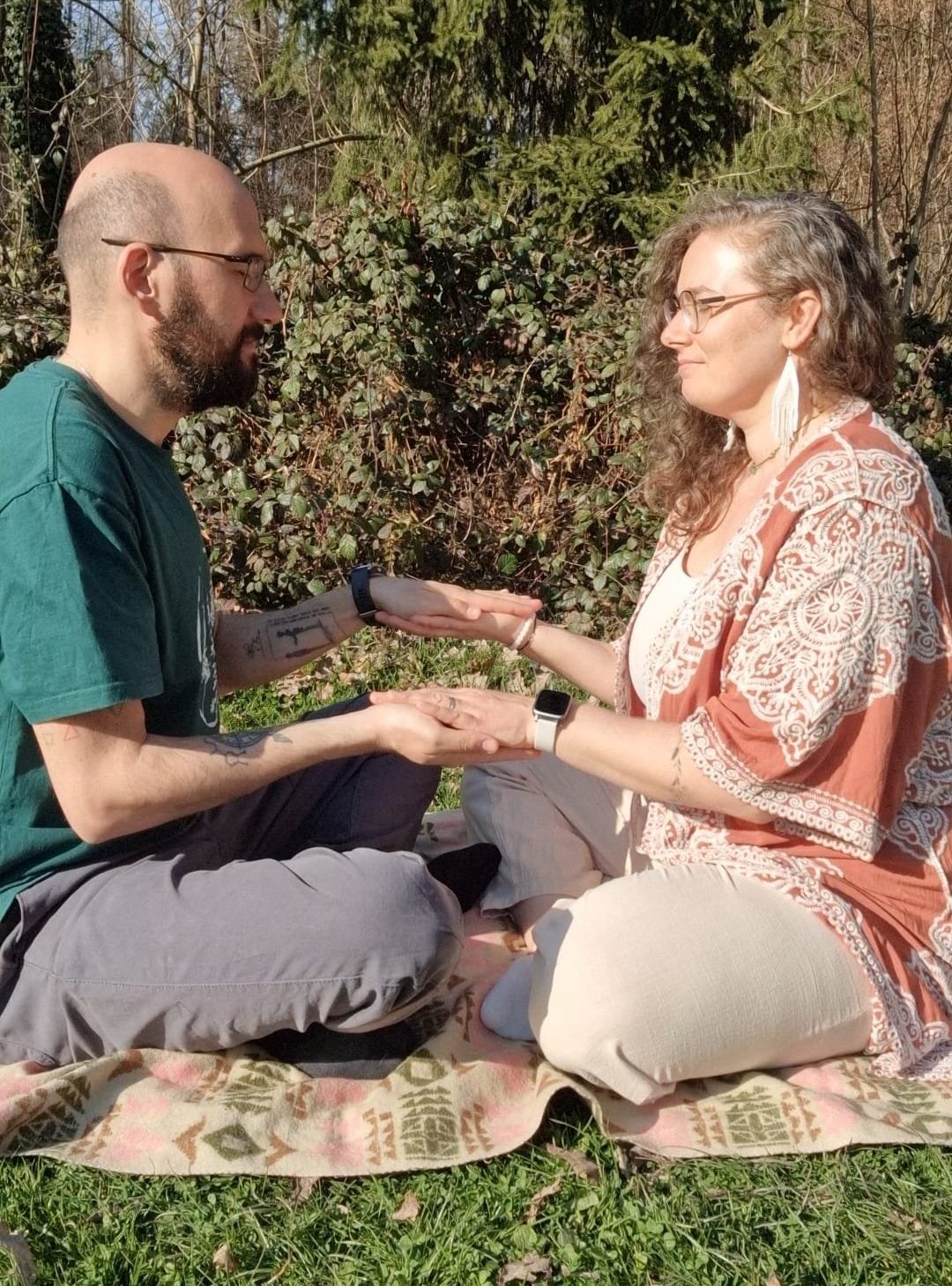 Two people sitting face to face in nature, hands joined in practice