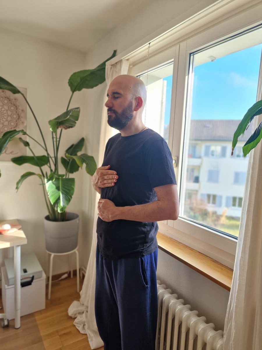 Flavius standing by the window with hands on chest and abdomen